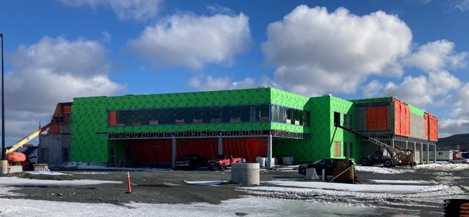 A green building in a construction zone, with snow on the ground and blue sky with some clouds.